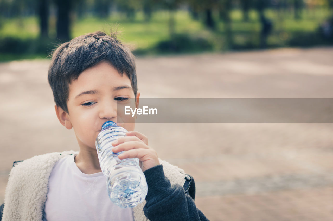 Close-up of boy drinking water while standing at park