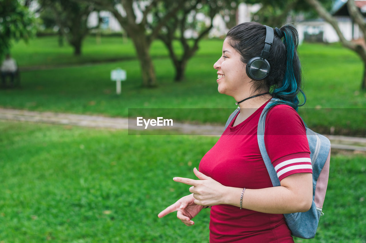 Beautiful college woman with blue hair and a red dress, listening to music with her wireless 