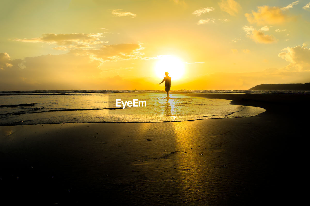 Silhouette man standing on beach against sky during sunset