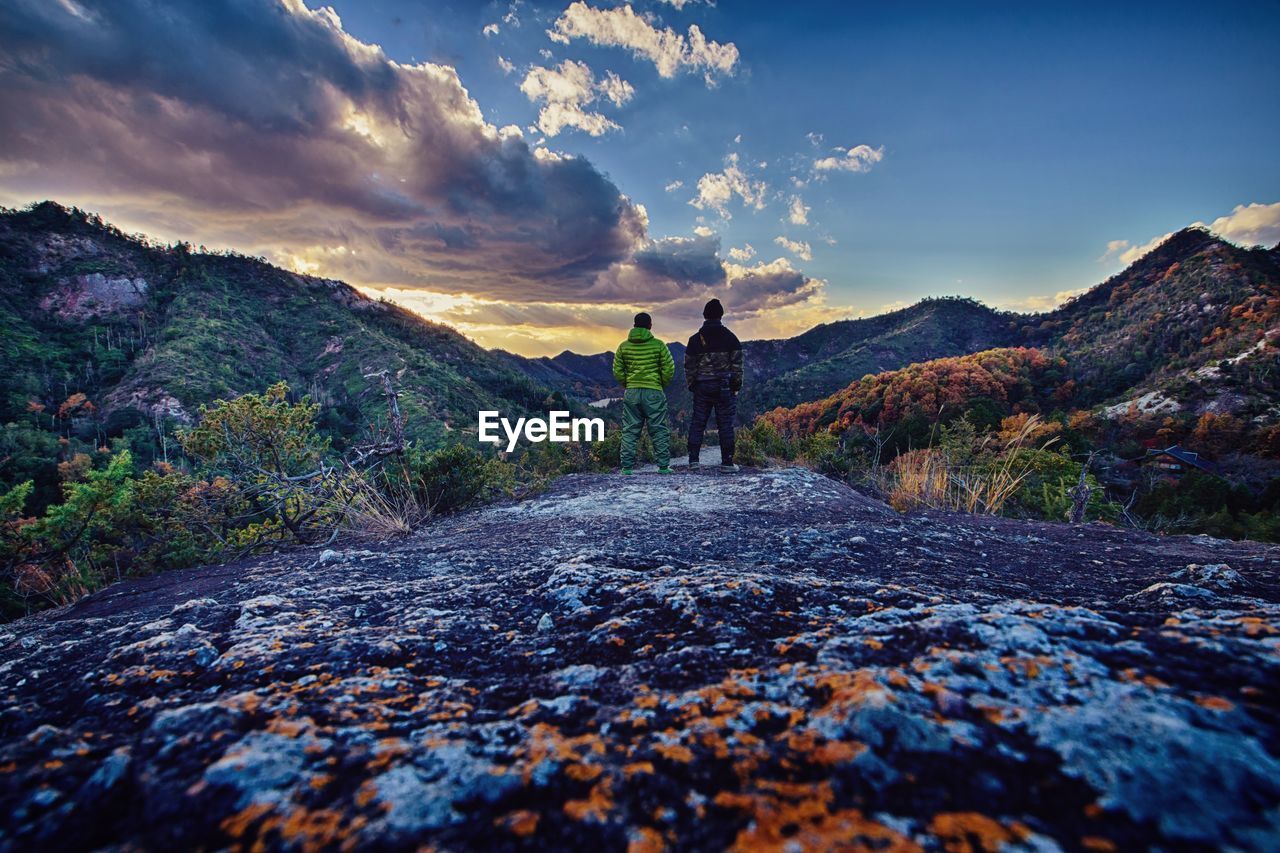 Rear view of people standing on mountain against cloudy sky