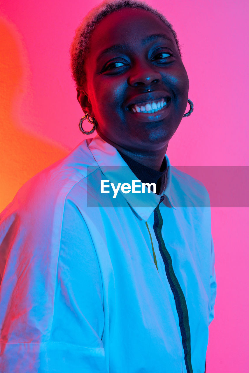 Delighted african american female smiling in studio with colorful neon lights and looking away