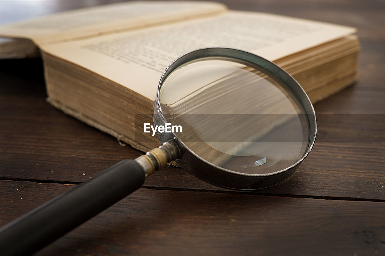 High angle view of magnifying glass with old book on table