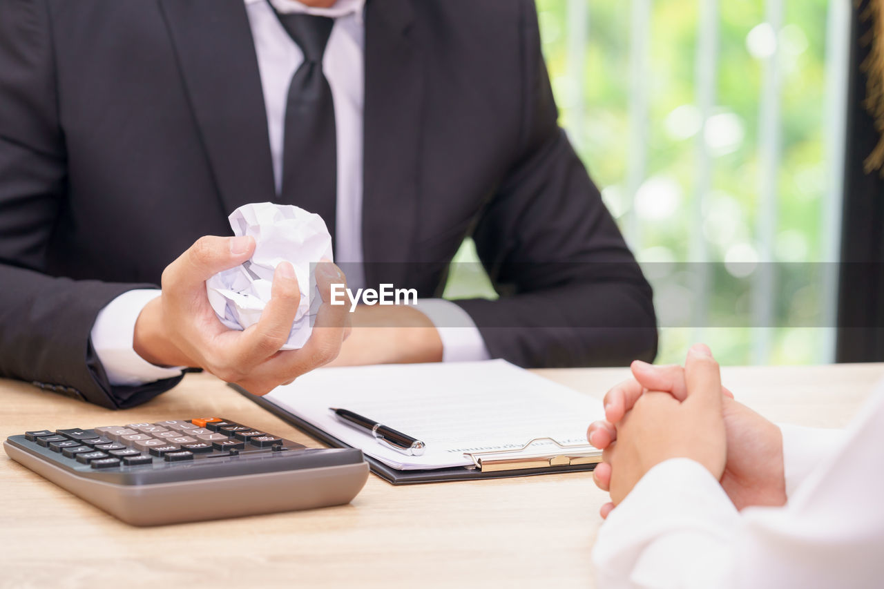 Midsection of businessman holding crumpled paper ball at desk in office