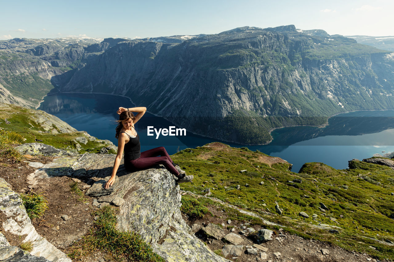 REAR VIEW OF PEOPLE SITTING ON ROCK AGAINST MOUNTAIN