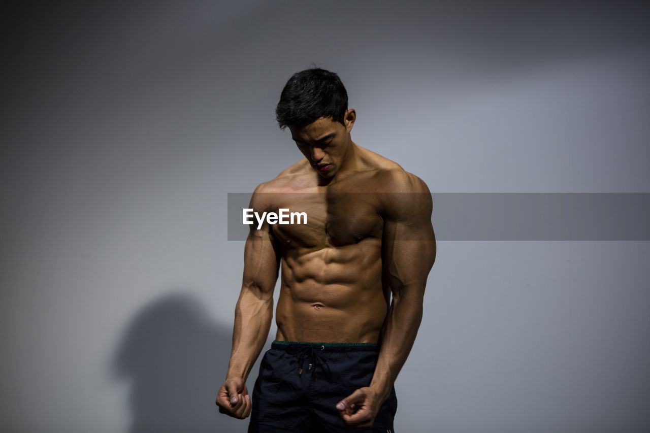 Close-up of shirtless man with muscular build over gray background