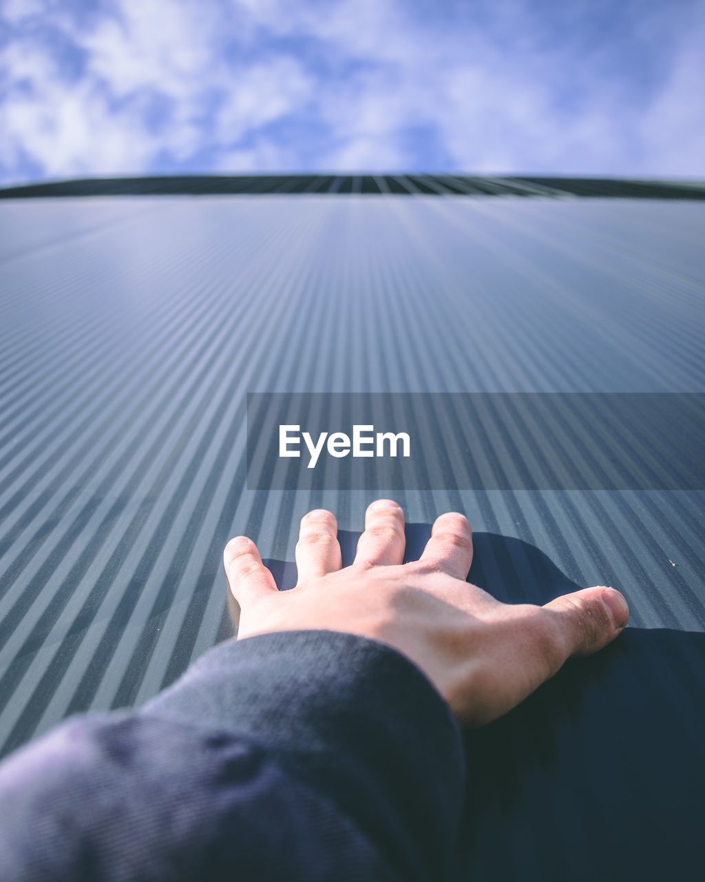 Low angle view of cropped hand touching building against sky