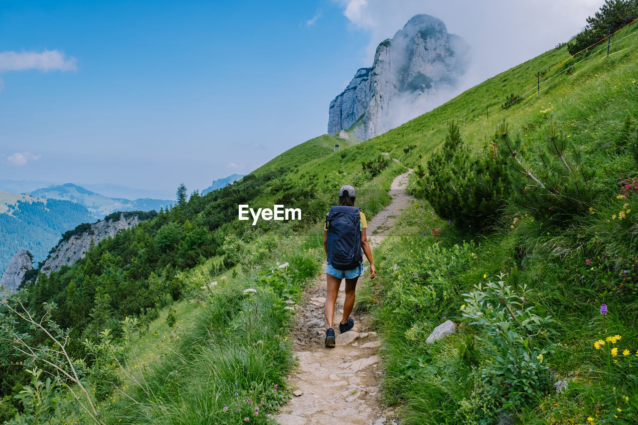 REAR VIEW OF MAN WALKING ON TRAIL AGAINST MOUNTAIN