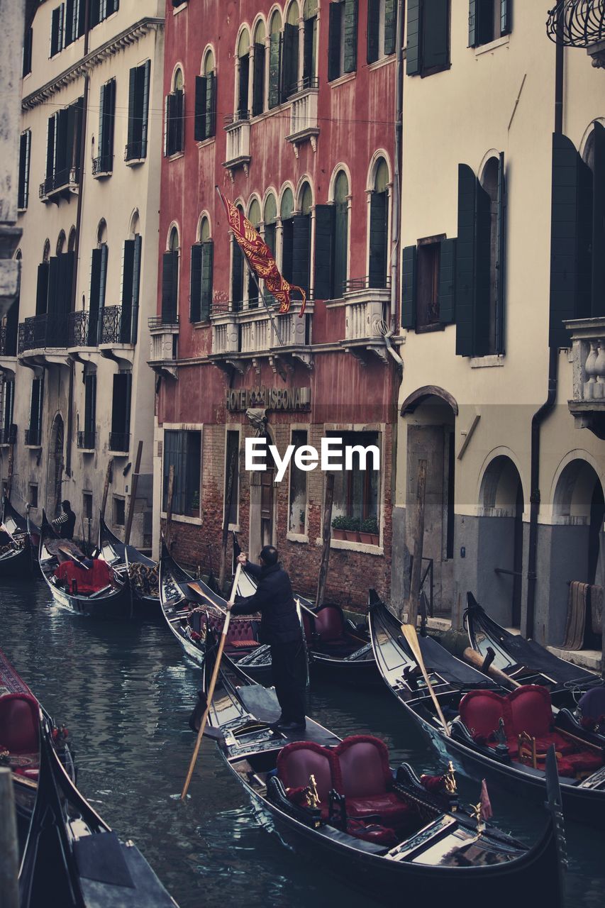 Rear view full length of man sailing gondola on canal by buildings