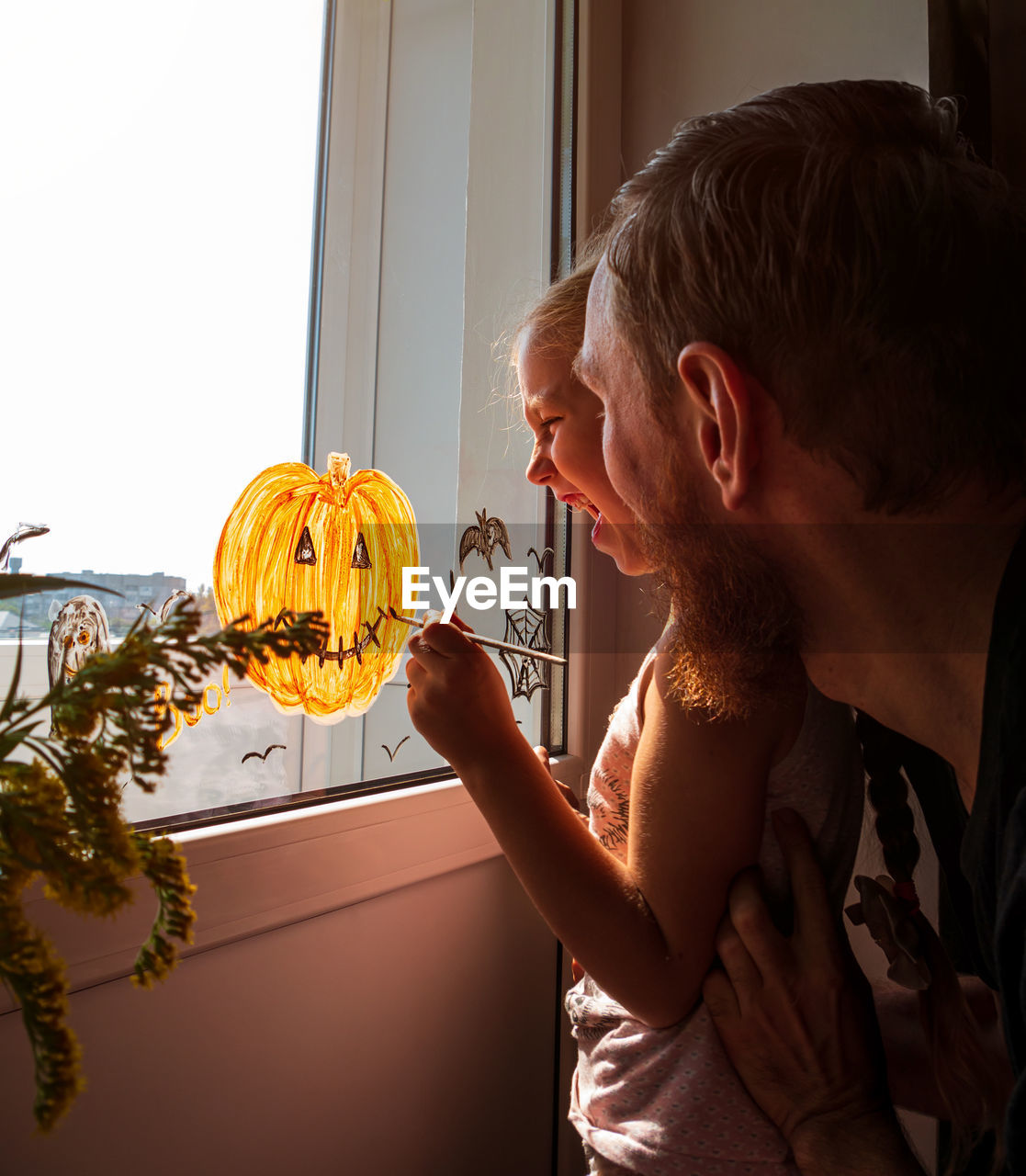 Child and father painting pumpkin on window preparing halloween little girl with dad decorating room