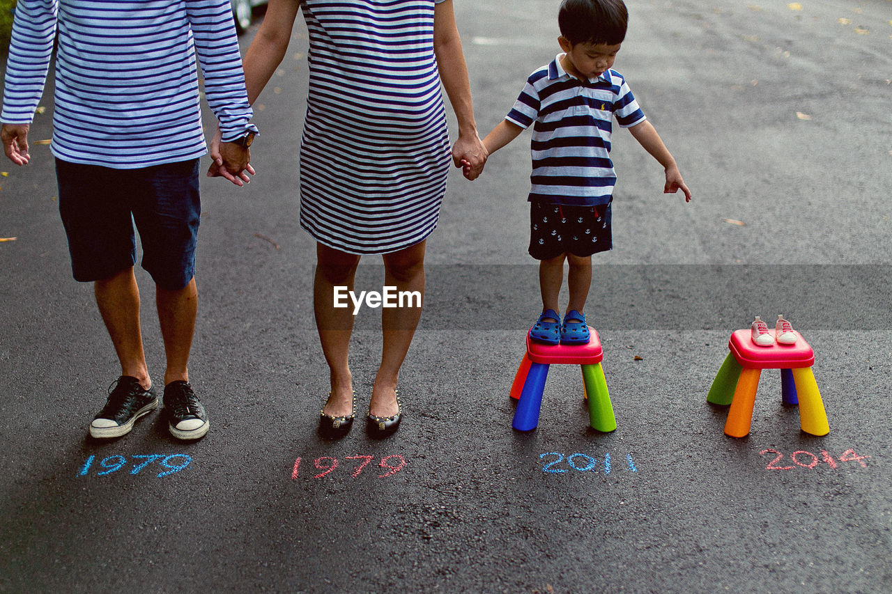 Expectant family of three standing by baby booties with years written on street