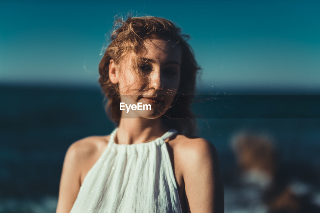 Close-up of young woman standing against sea