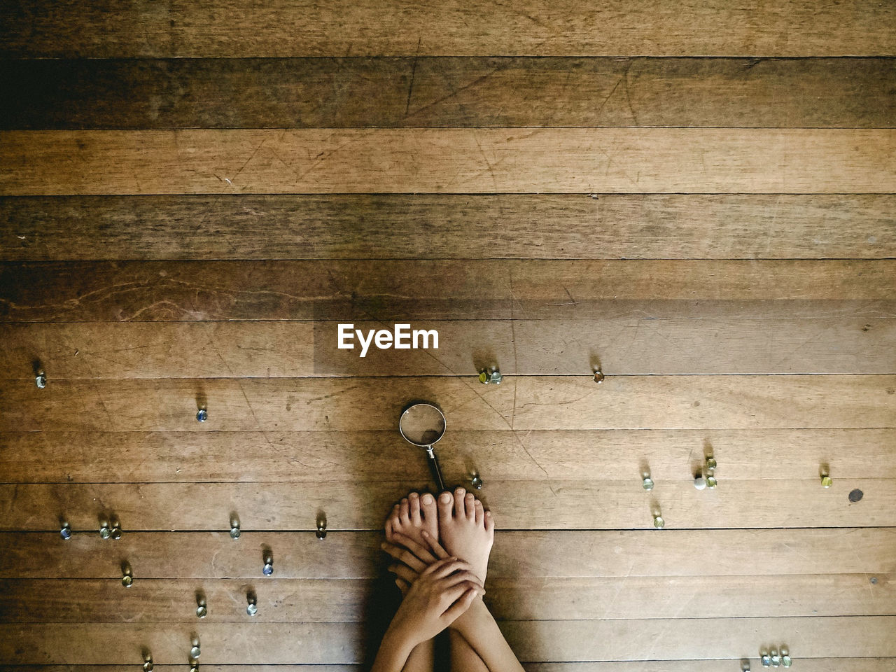 Cropped image of person crouching with marbles and magnifying glass on hardwood floor