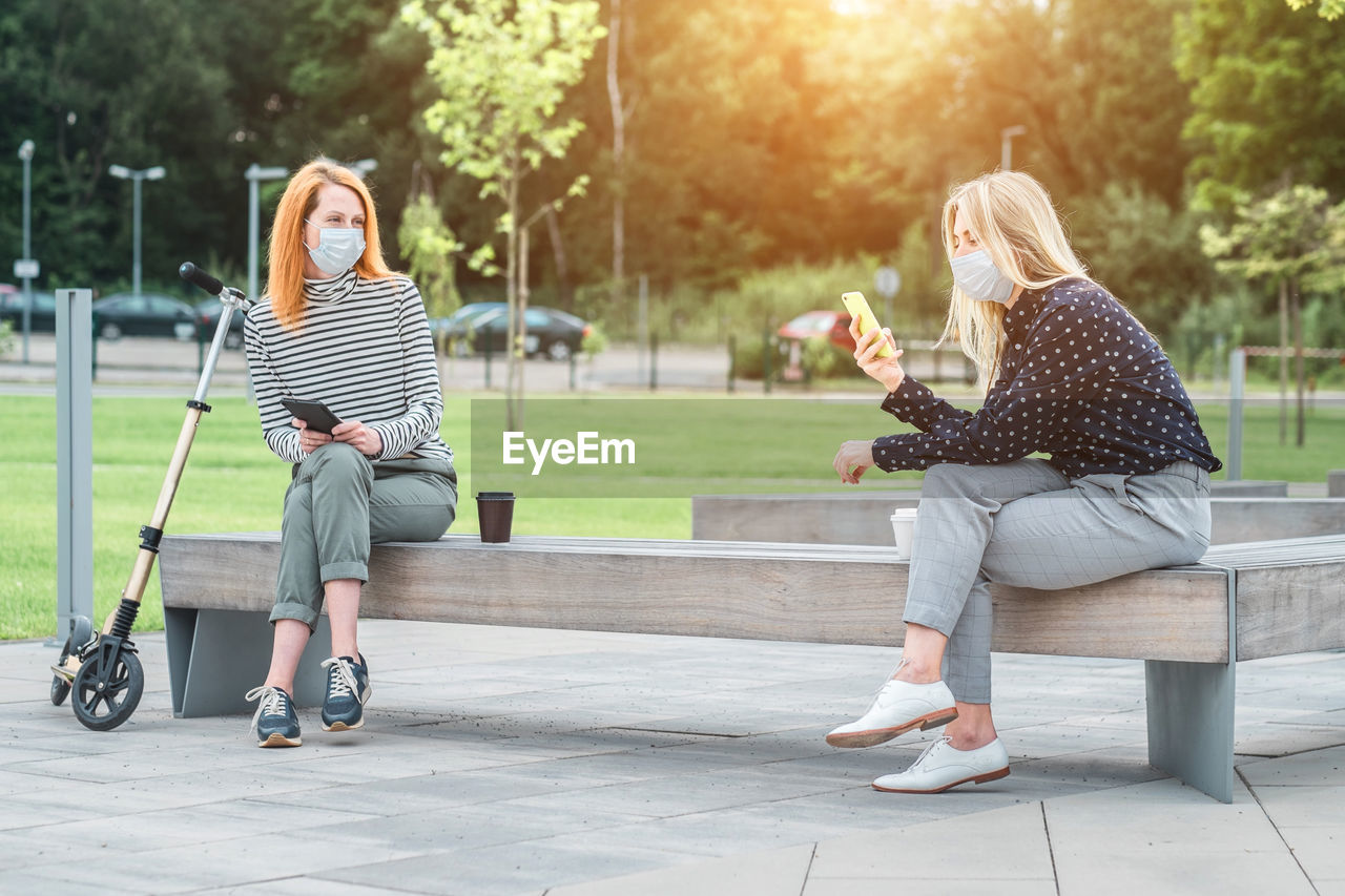 Female colleagues wearing masks working on tablet, while sitting in town. long distance communicate.