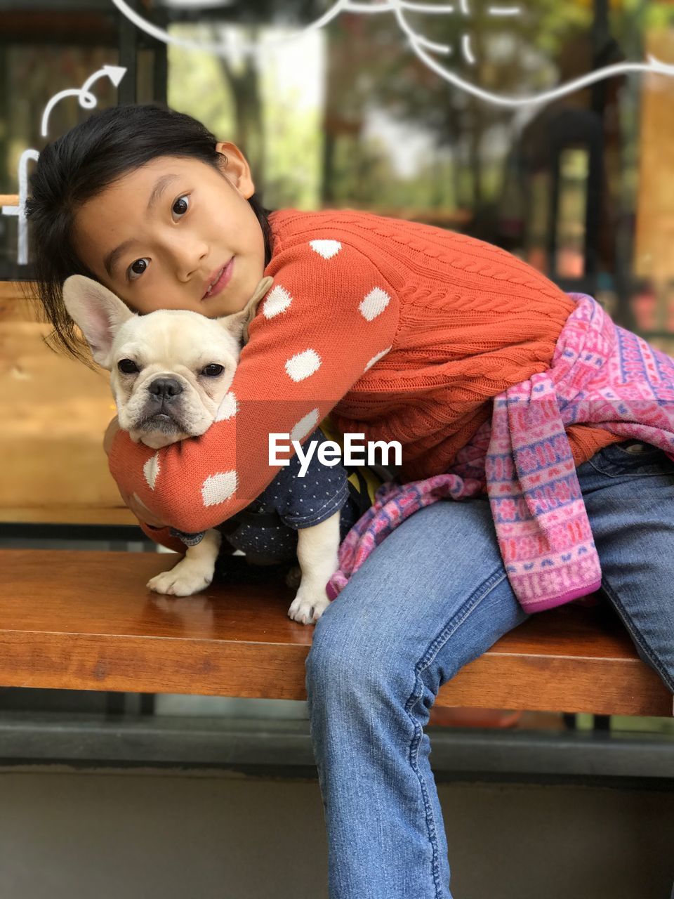 Portrait of cute girl embracing dog while sitting on bench