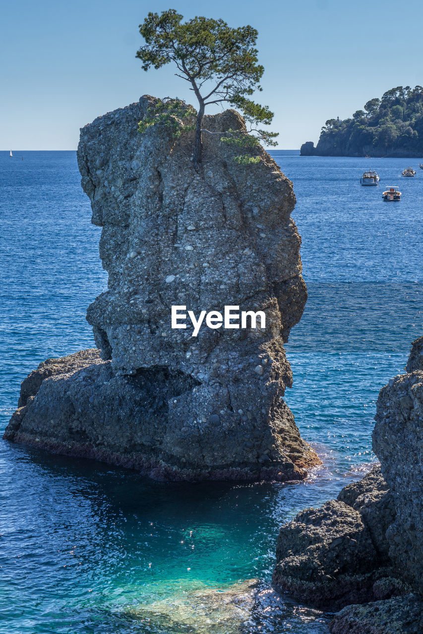 Rock formation by sea against clear blue sky