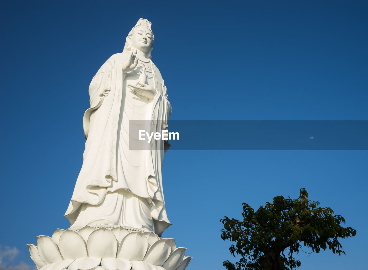 Low angle view of lady buddha against clear blue sky