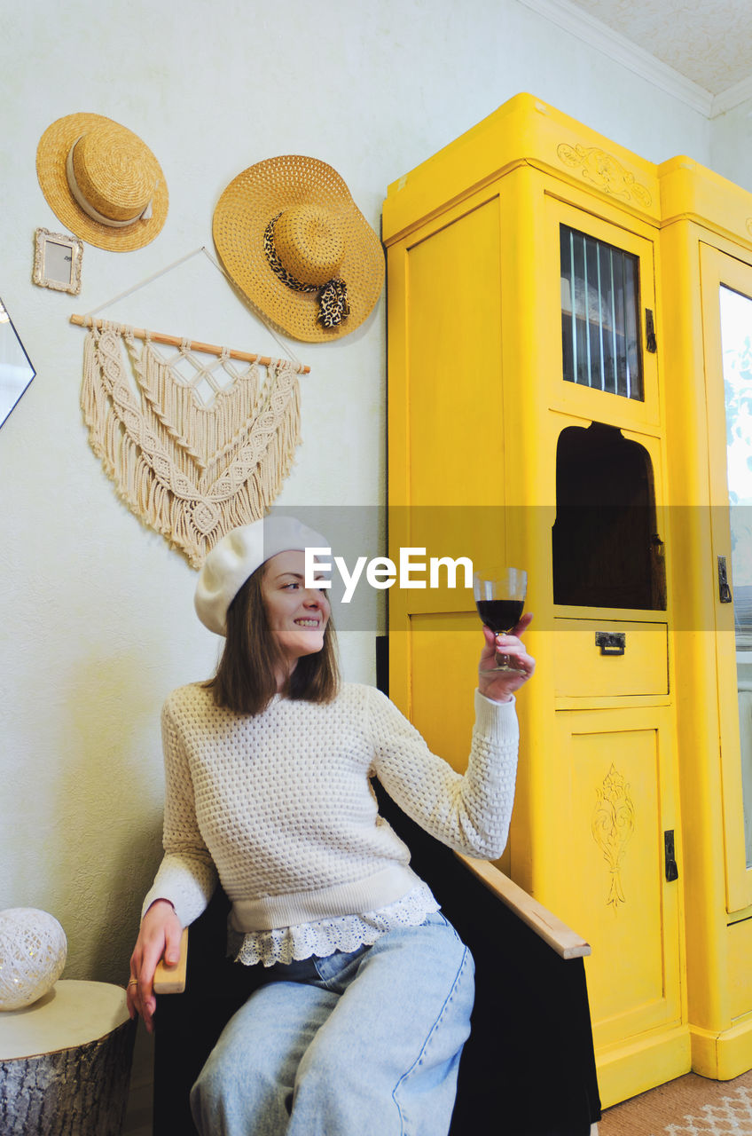 Young woman in beret sits in cozy home, room with music record in hands. vintage yellow cabinet.
