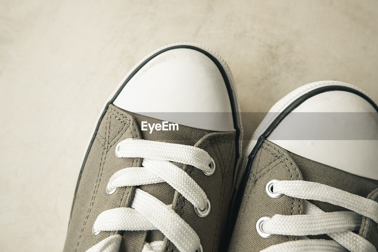 LOW SECTION OF PERSON WEARING CANVAS SHOES ON TILED FLOOR