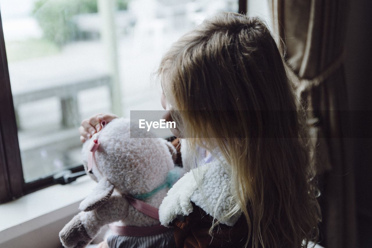 High angle view of girl holding stuffed toy against window