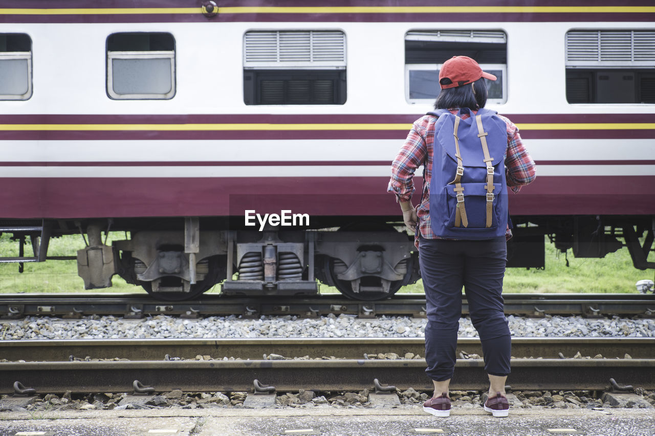 REAR VIEW OF MAN STANDING AT RAILROAD STATION