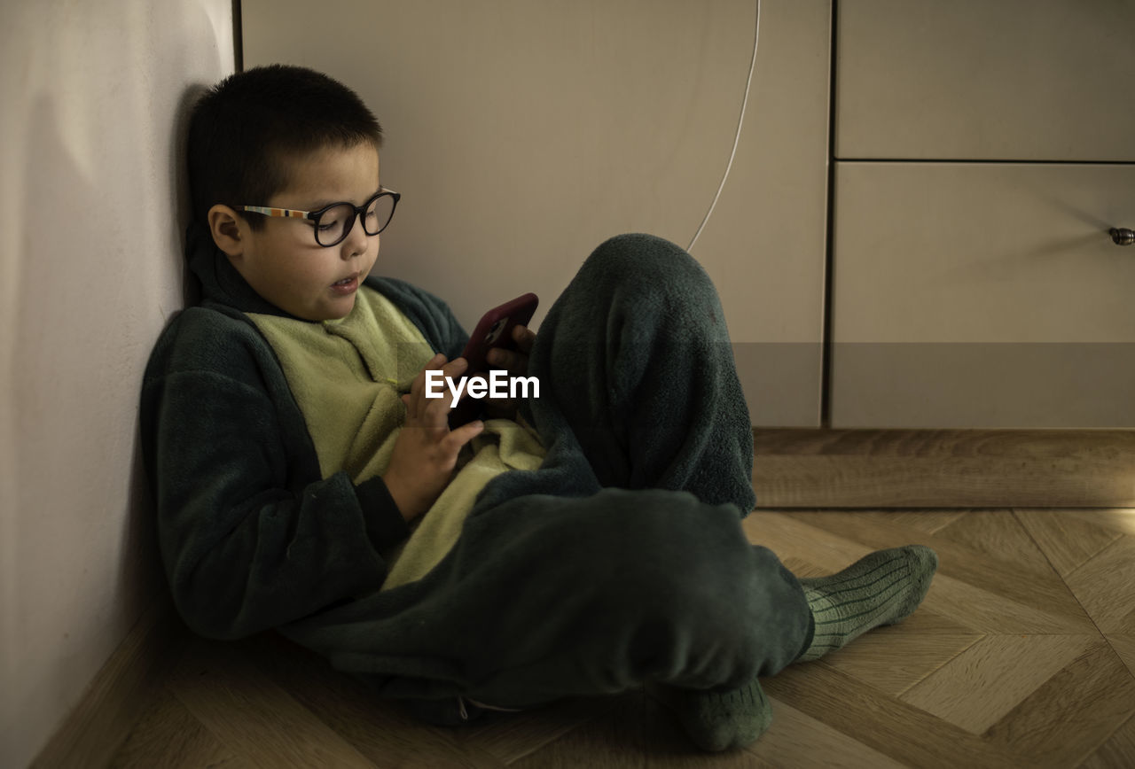 Closeup portrait of a boy who looks into the phone sitting on the floor, phone charging