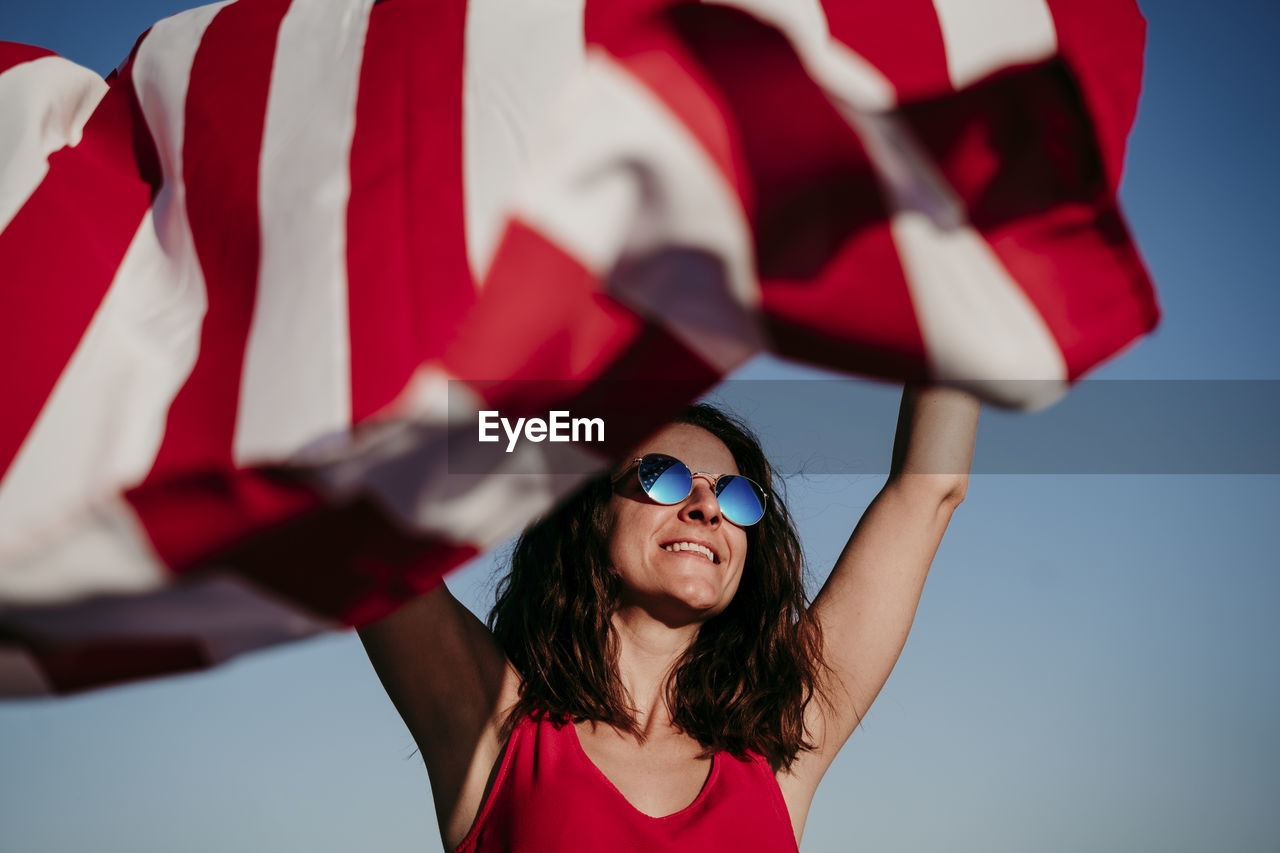 Woman waving flag against blue sky