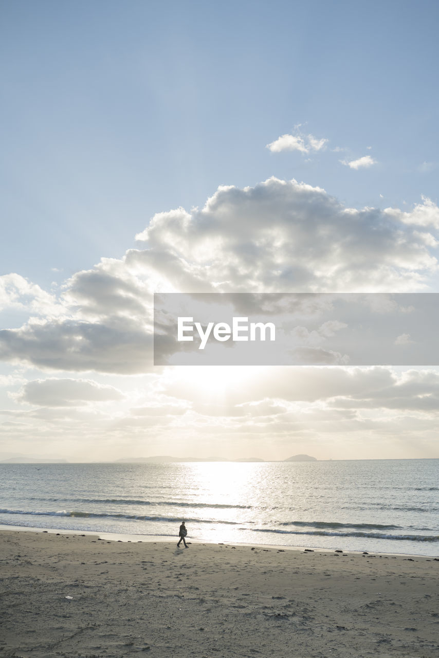 Person walking at beach against sky during sunset