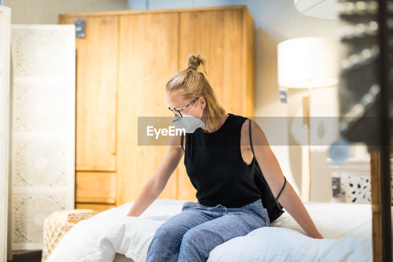 Woman wearing flu mask sitting on bed at store