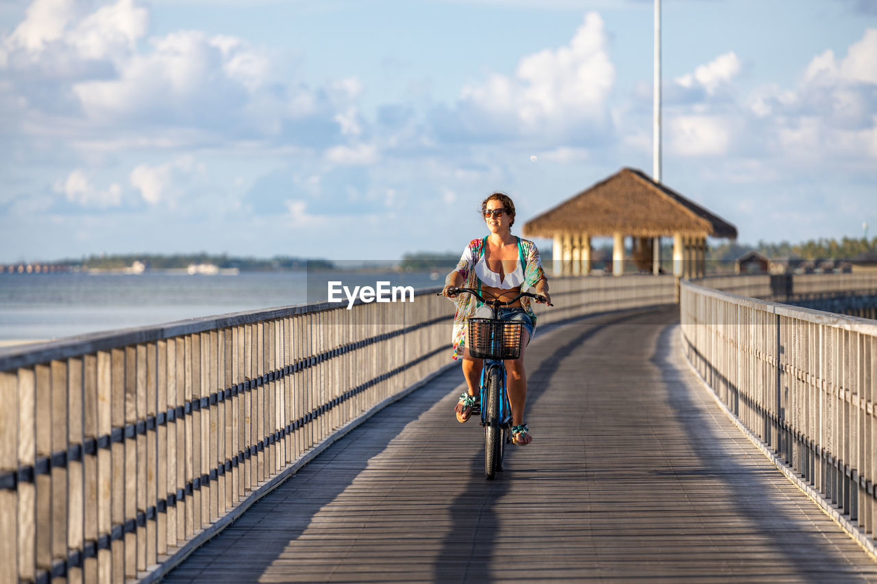 Middle aged woman riding a bicycle on a pathway near the ocean