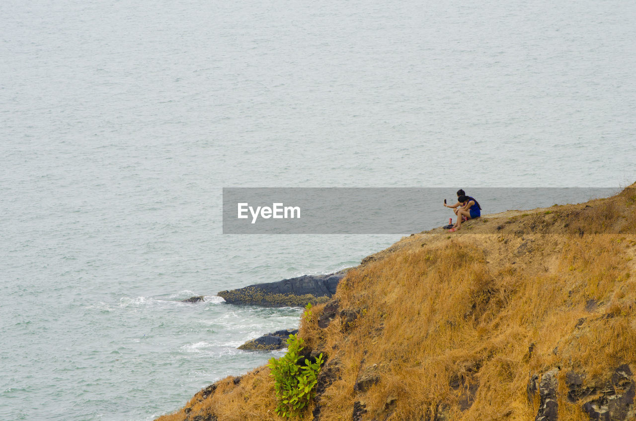People sitting on rock formation by sea