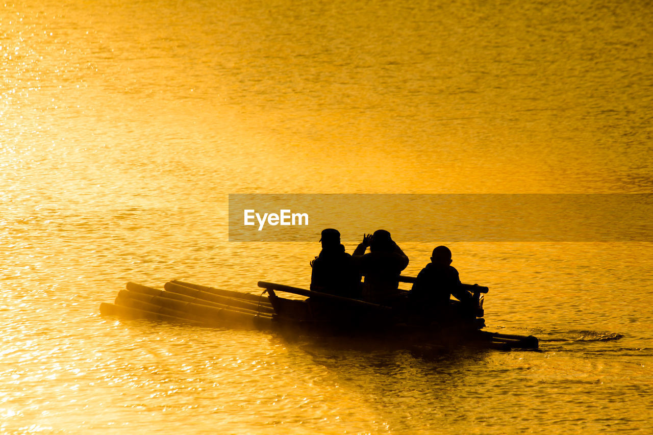 Silhouette people sailing in sea during sunset