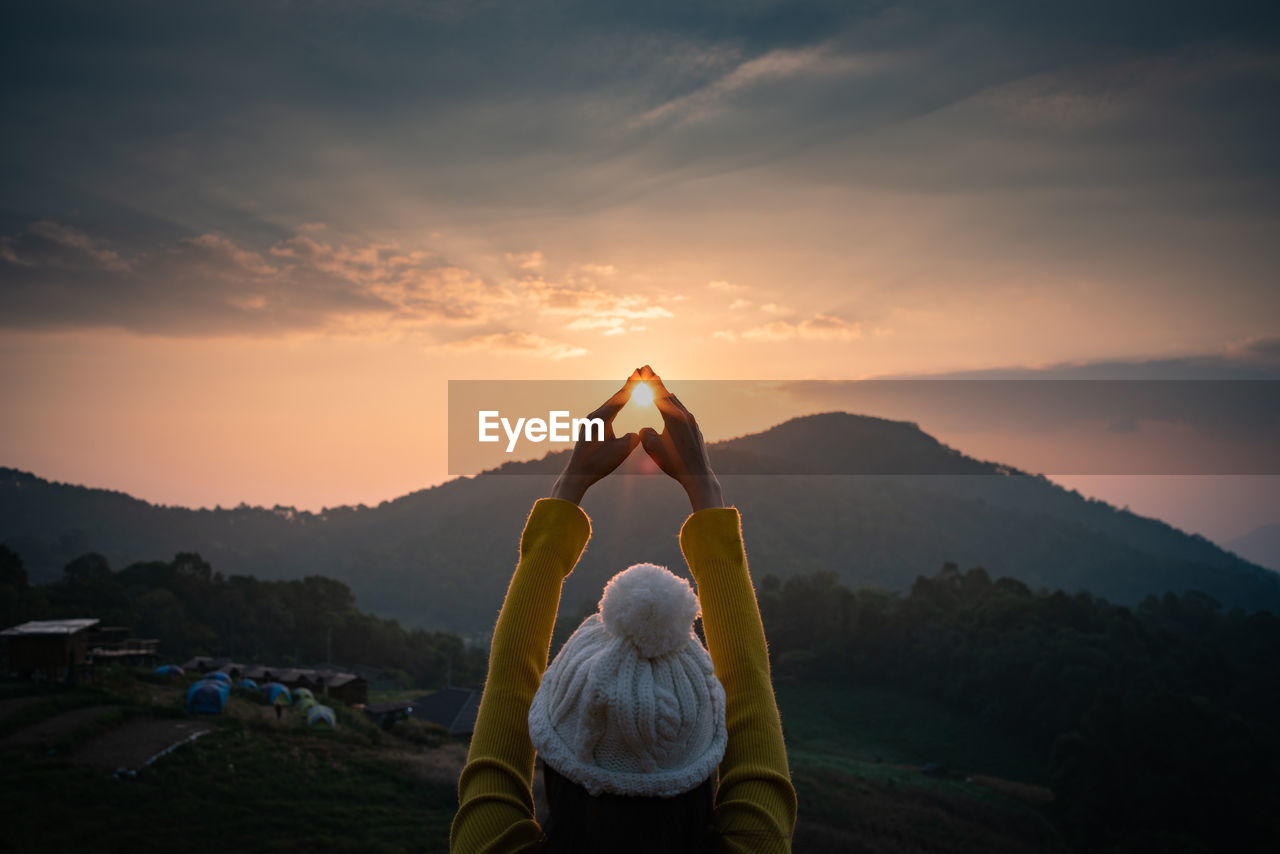 Rear view of woman gesturing against sky during sunset