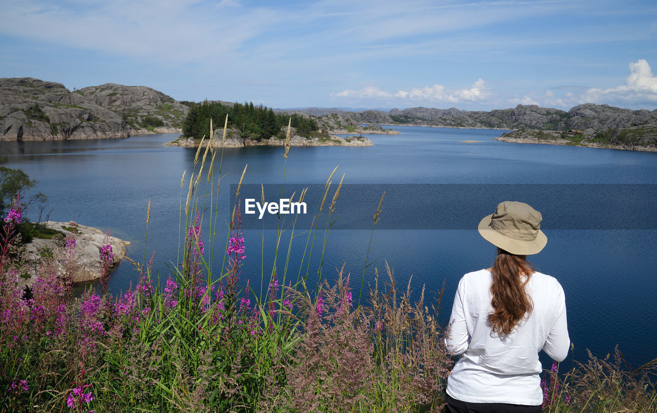 Rear view of woman standing by lake against sky