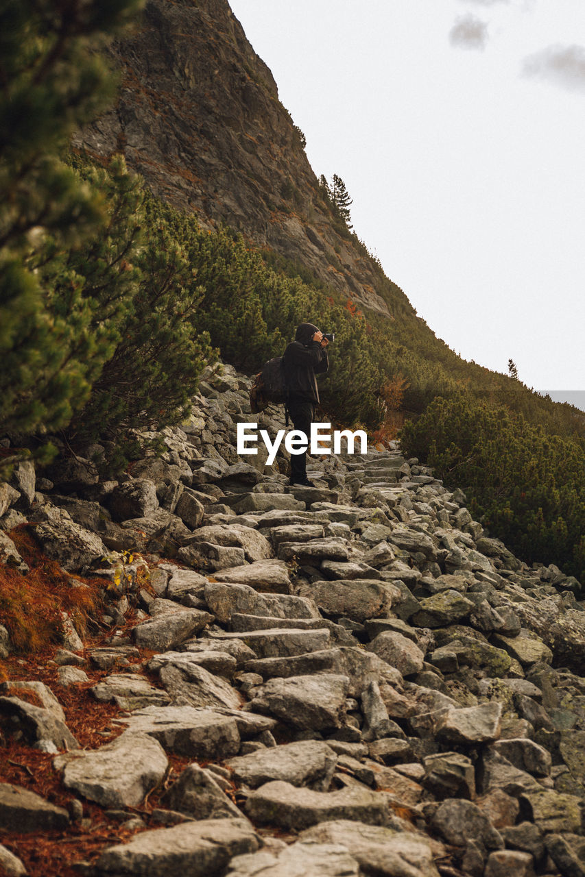 Rear view of man standing on rock against sky