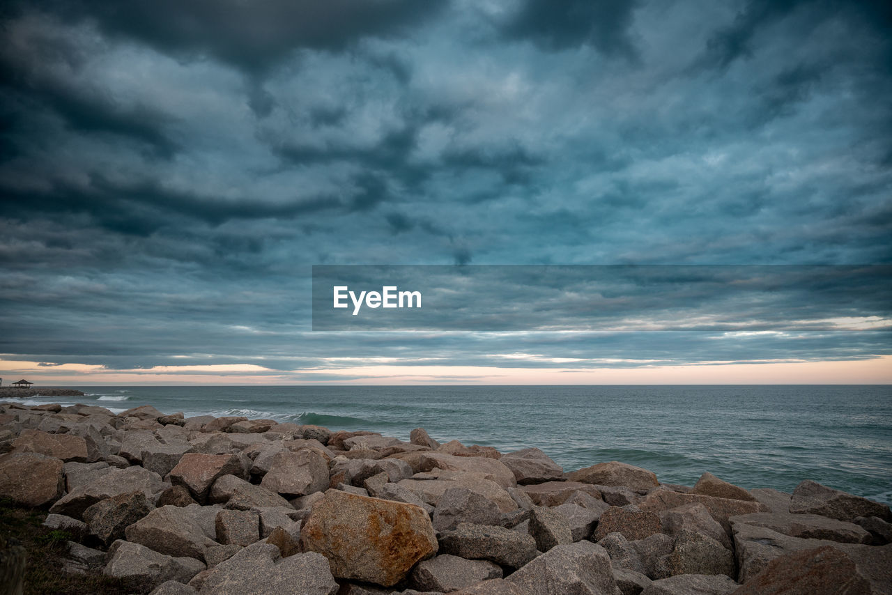 cloud, sky, sea, horizon, water, rock, ocean, beach, land, nature, beauty in nature, scenics - nature, coast, shore, environment, dramatic sky, wave, horizon over water, storm, sunlight, sunset, cloudscape, dusk, storm cloud, seascape, landscape, no people, overcast, tranquility, outdoors, coastline, body of water, travel destinations, tranquil scene, travel, water's edge, evening