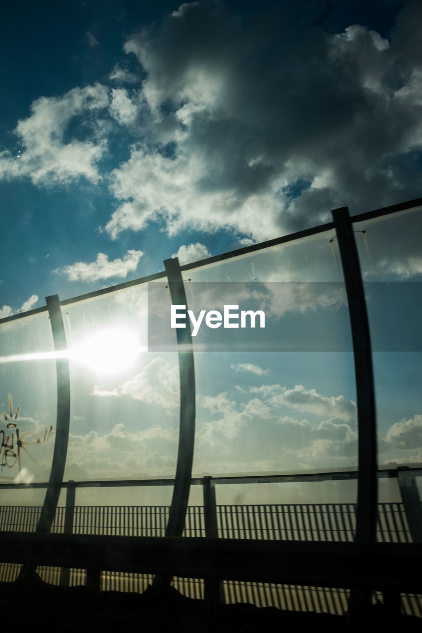 sky, cloud, sunlight, nature, light, reflection, architecture, railing, no people, built structure, lens flare, darkness, silhouette, bridge, sunbeam, outdoors, fence, sunset, low angle view, back lit, horizon, evening, sun, dusk, day, line, beauty in nature, metal, water