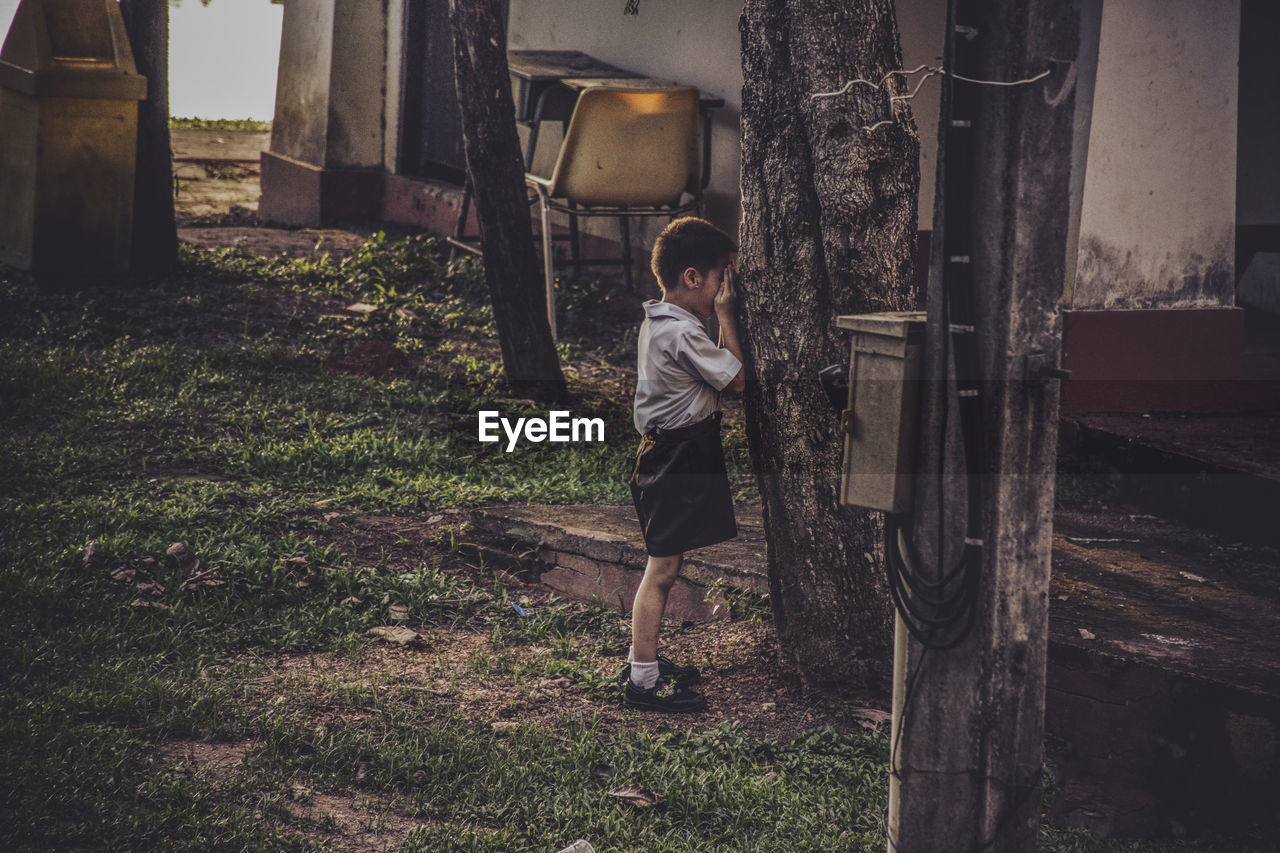 Boy playing hide and seek behind tree trunk