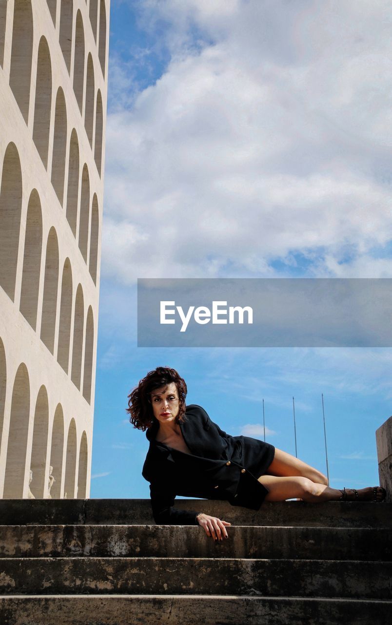 Low angle view of young woman looking at camera against sky