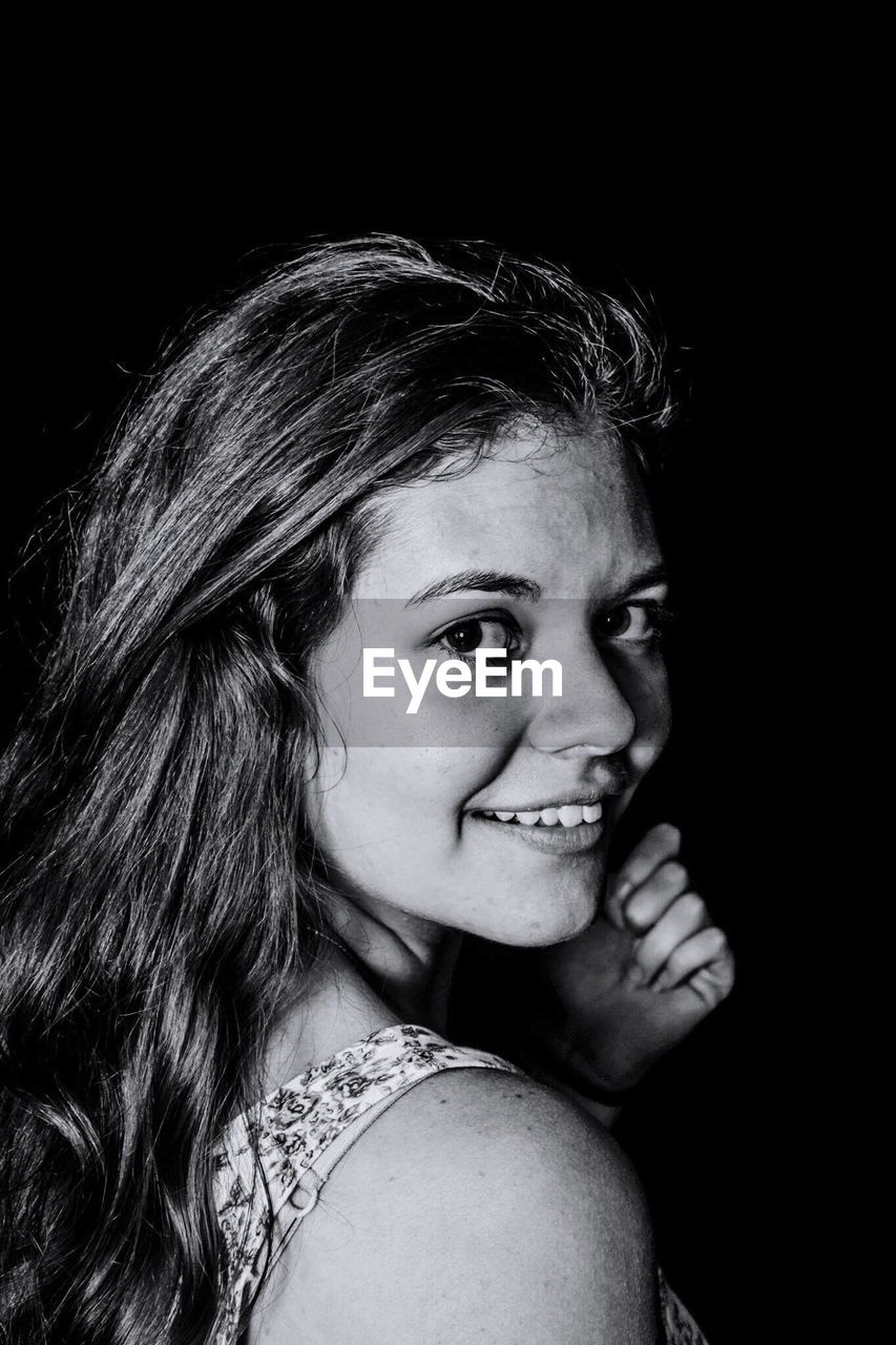 Portrait of smiling young woman against black background