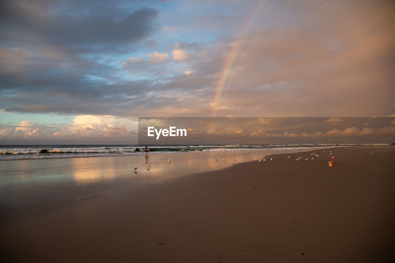Scenic view of beach against sky during sunset and rainbow