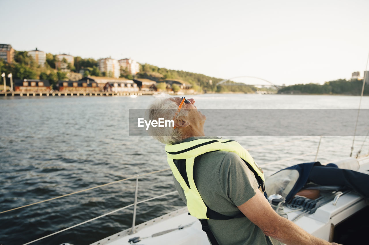 Senior man laughing in boat against sky on sunny day