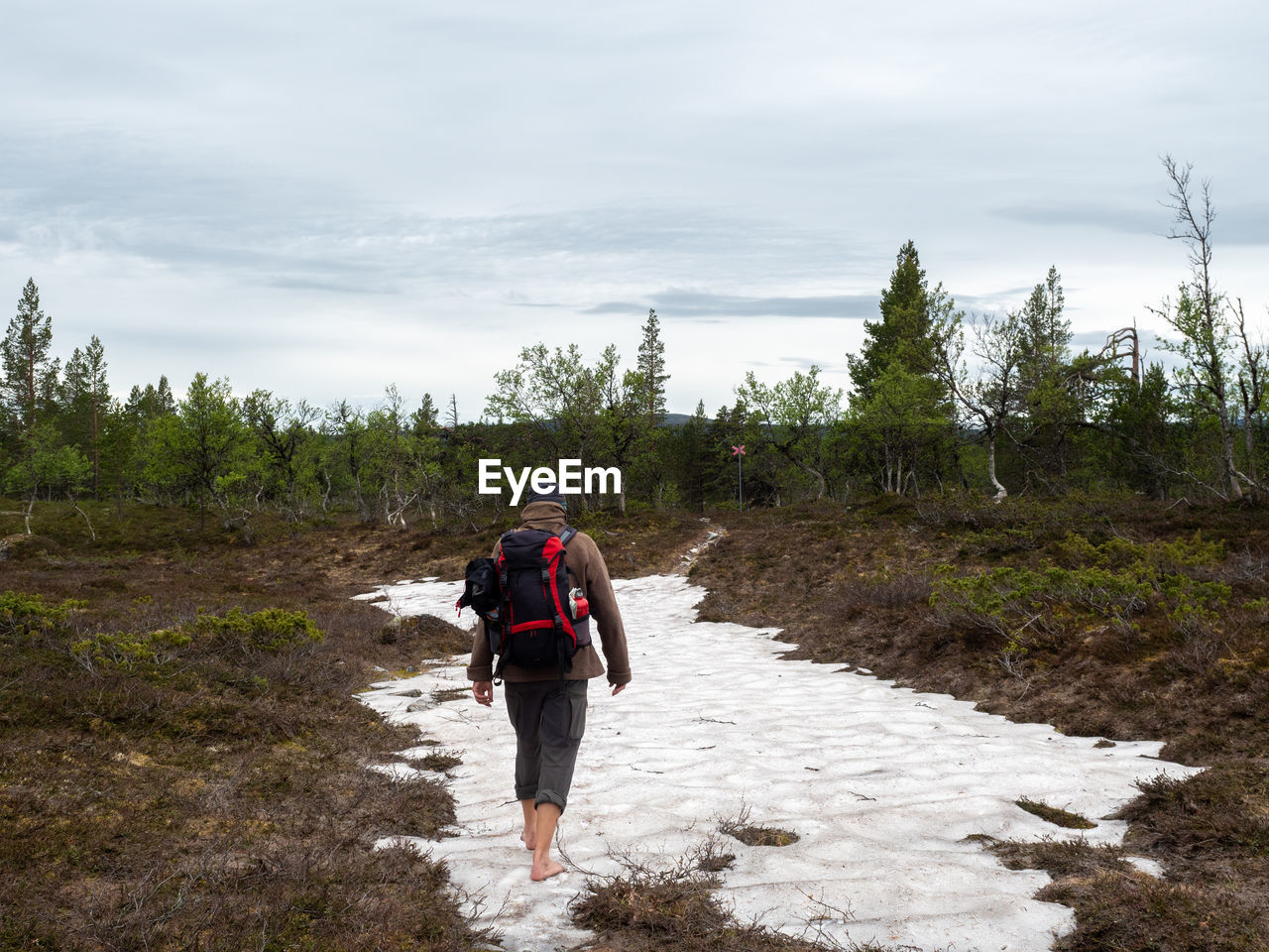 Rear view of man walking on snow against sky