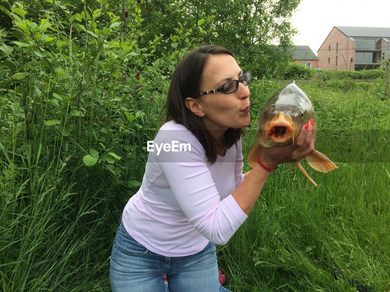 Happy woman kissing fish on grassy field