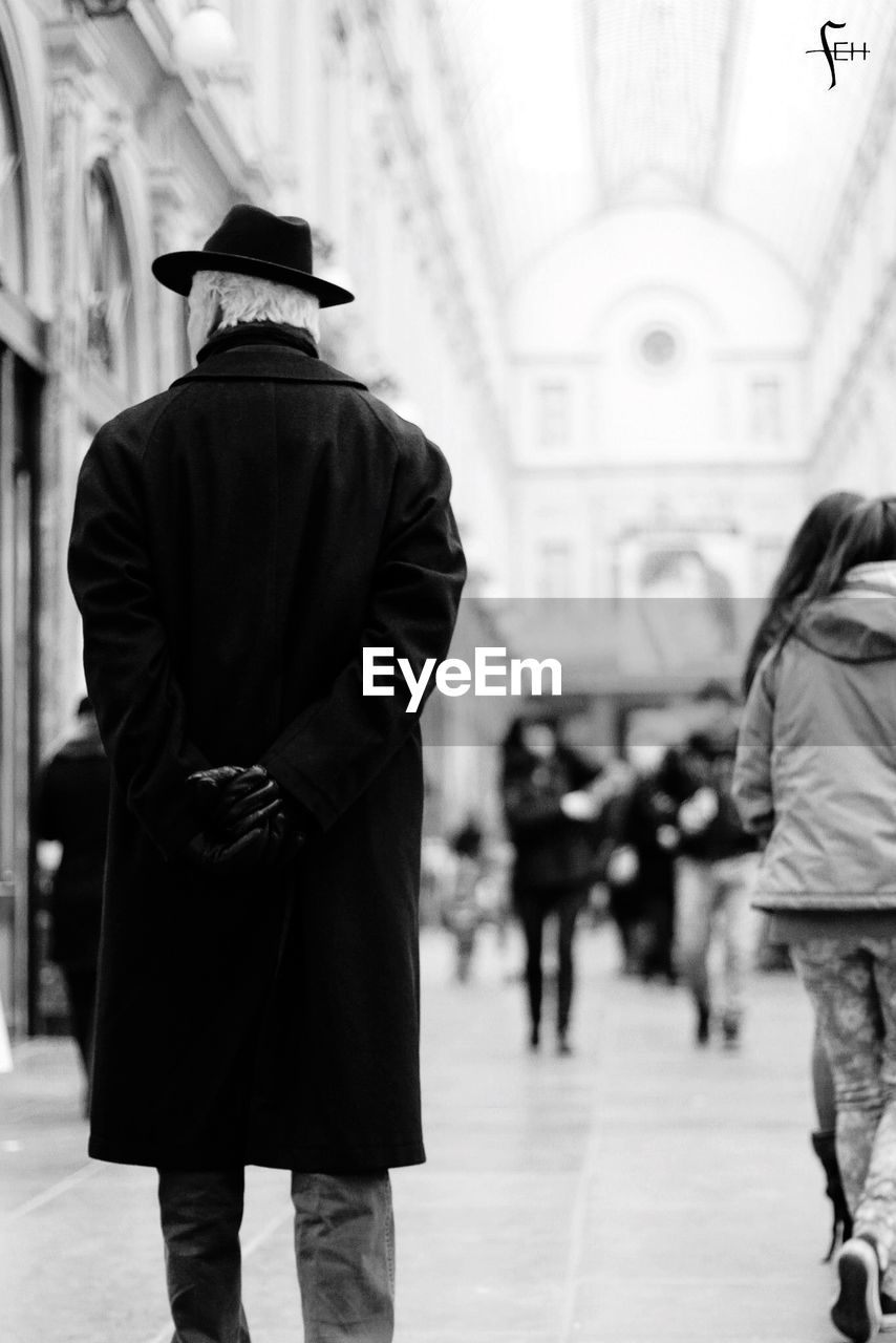 Rear view of senior man in long coat walking in corridor