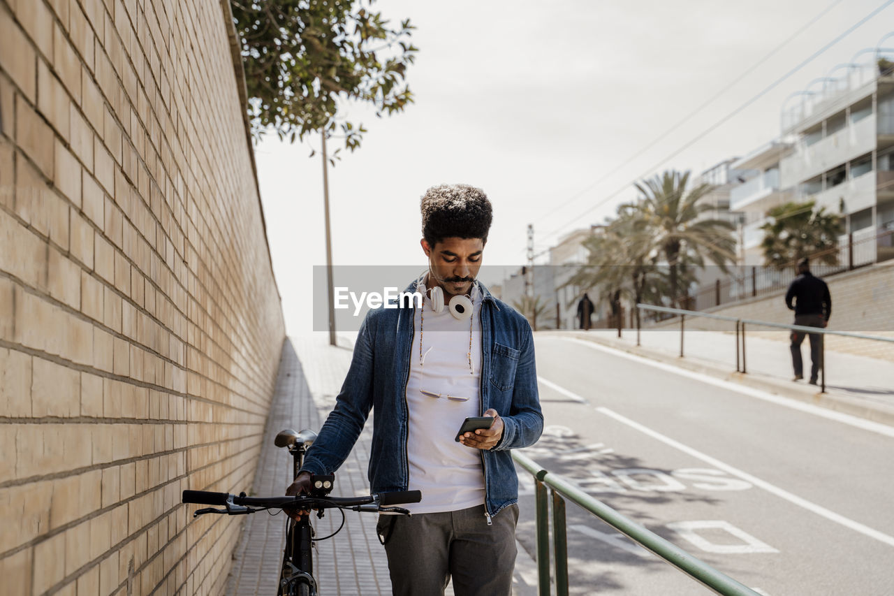 Handsome man using mobile phone while standing with bicycle on footpath