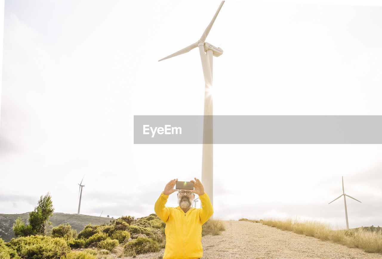 Man taking selfie near wind turbines at sunset