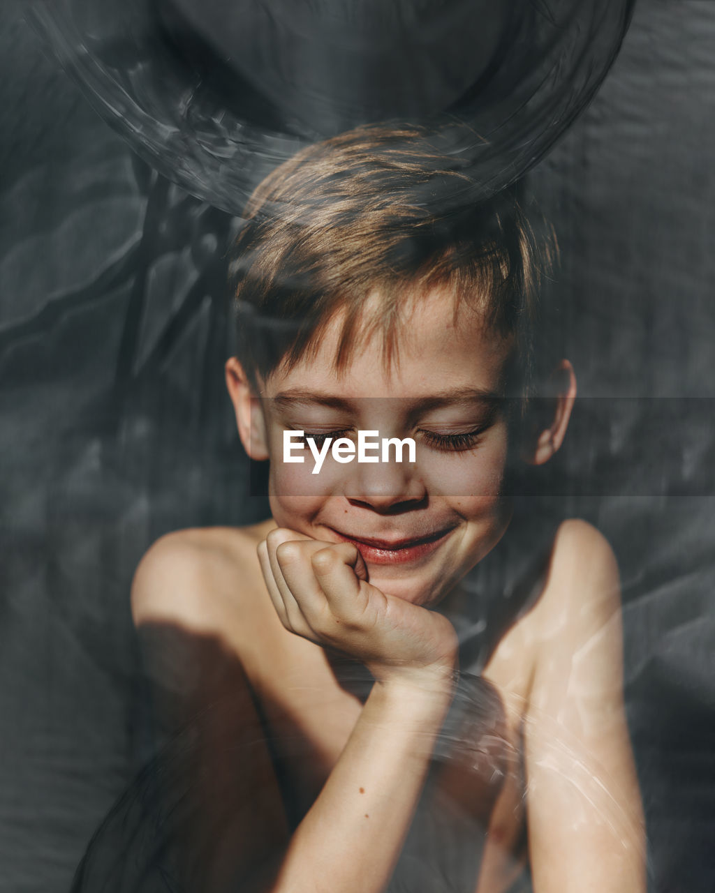 Close-up of shirtless boy smiling seen through glass