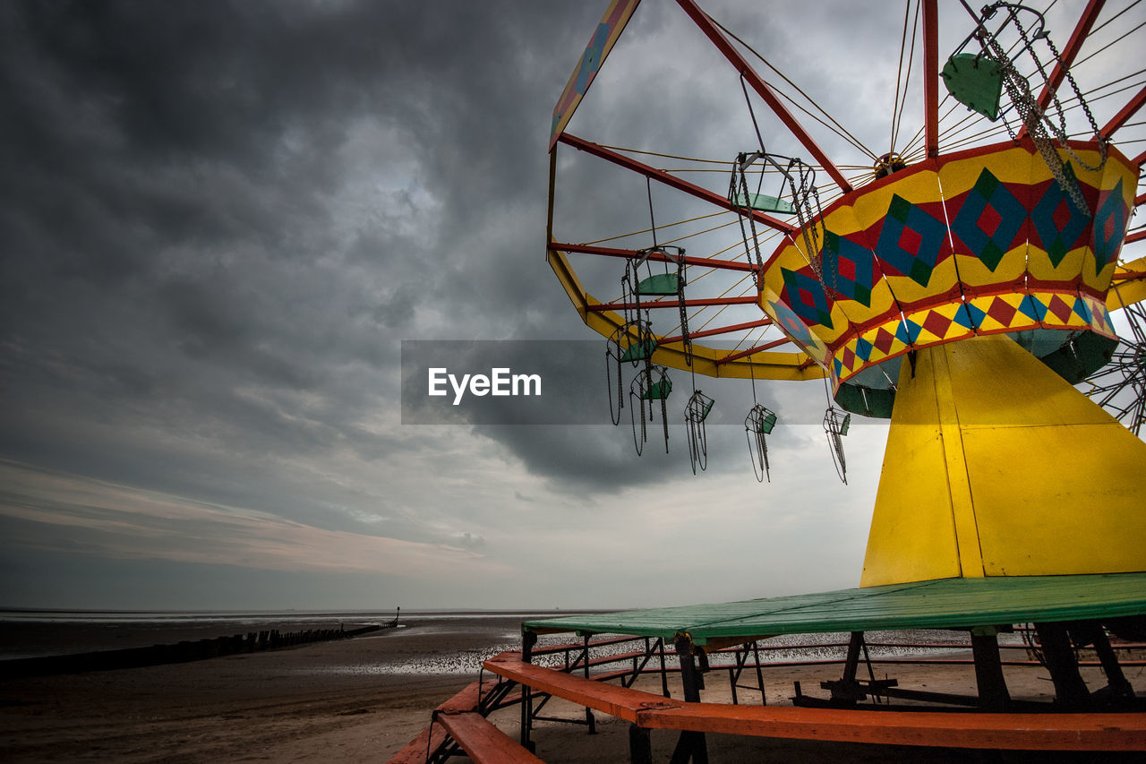 Chain swing ride on beach against cloudy sky