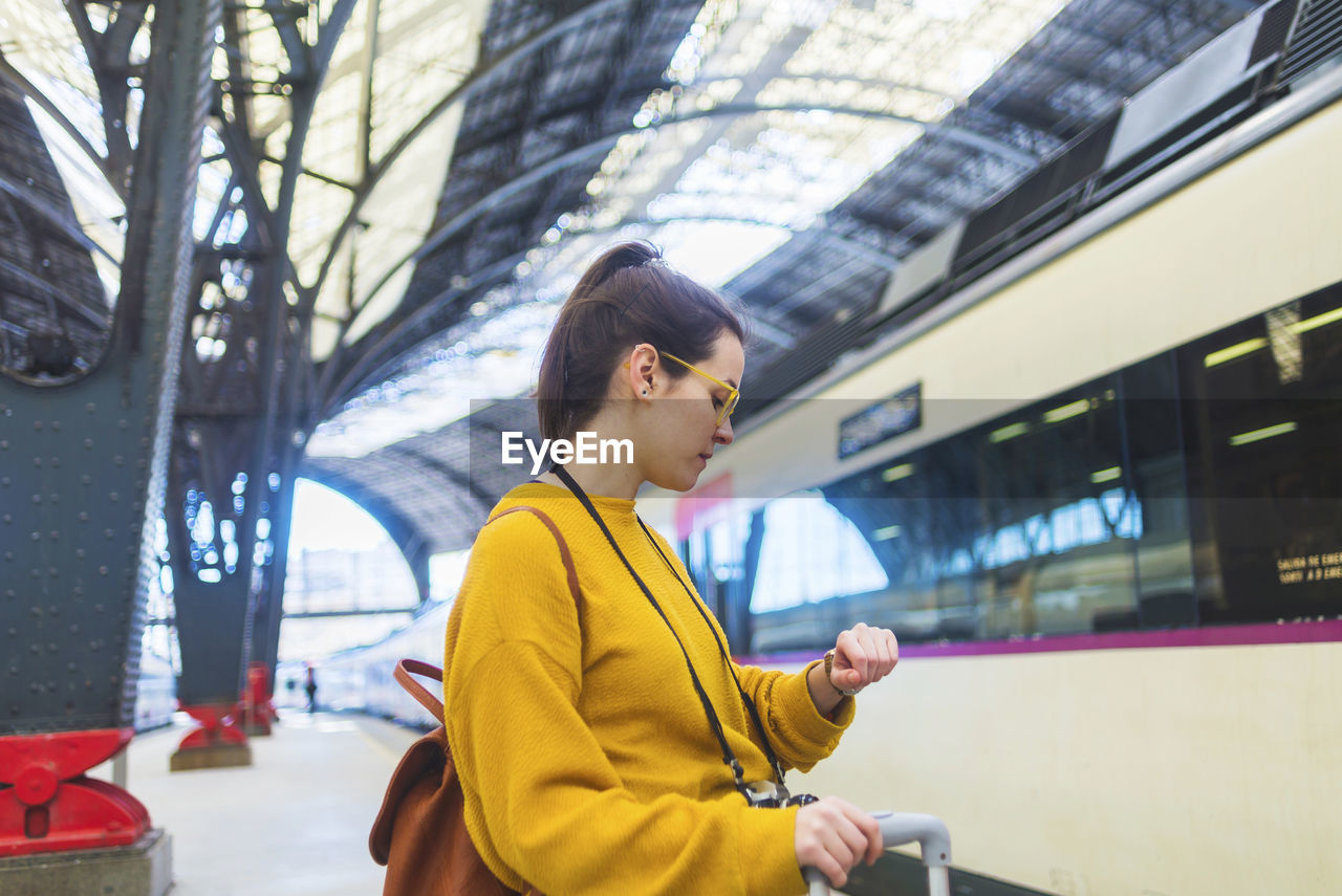 Side view of woman with luggage checking time while standing at railroad station platform