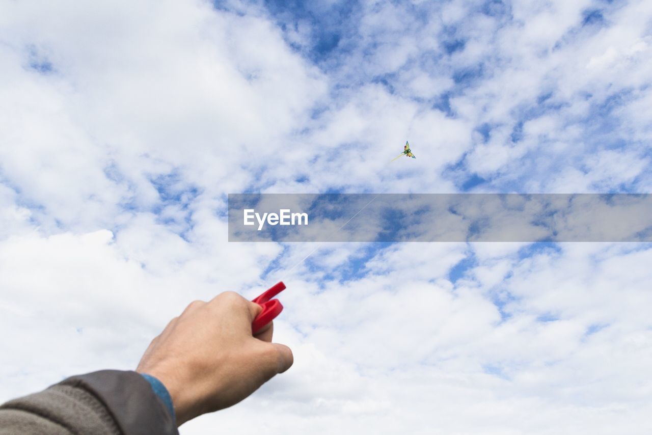 Low angle view of hand holding flying kite against sky